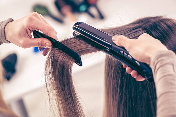 close up of a hairdresser straightening long brown hair with hair irons.