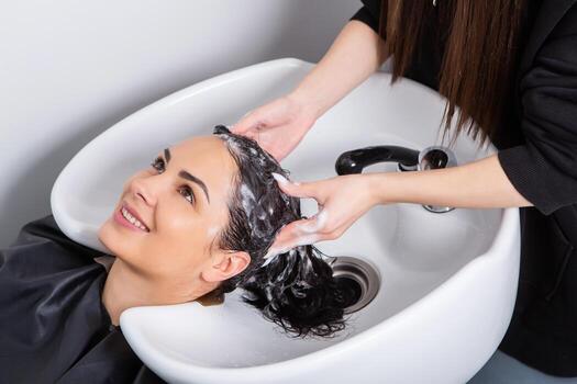 professional hairdresser washing hair of young woman in beauty salon photo